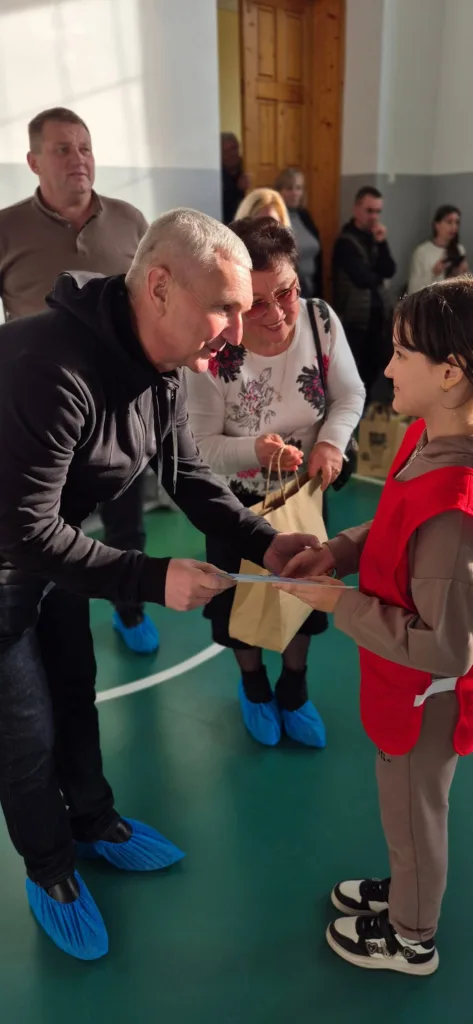 Чоловік вручає подарунок дитині у спортивній залі