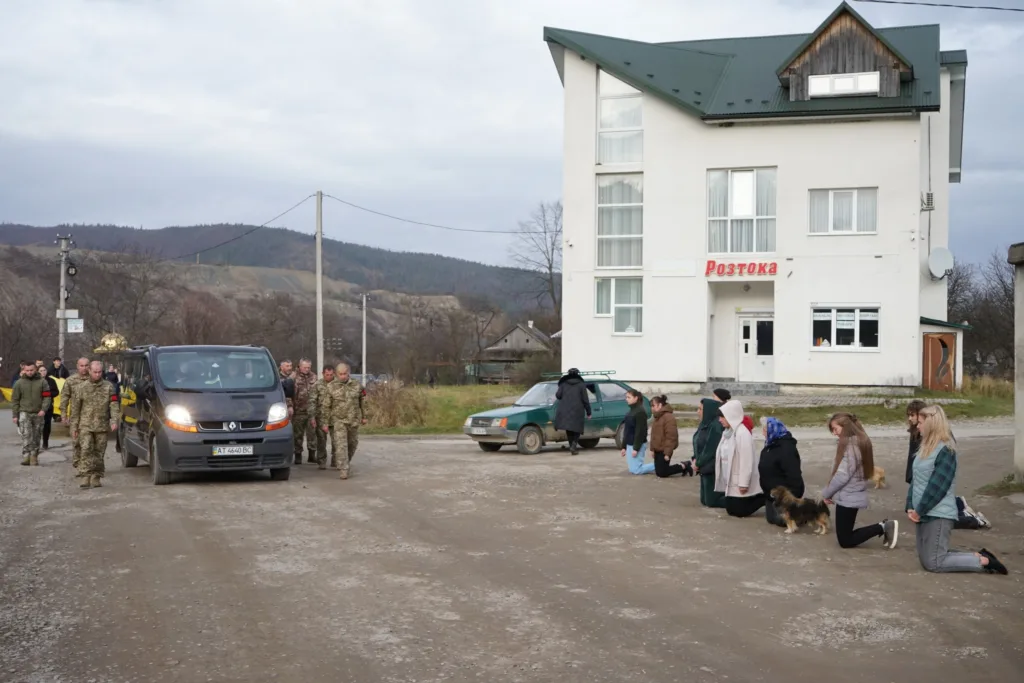 Люди на колінах зустрічають військовий кортеж