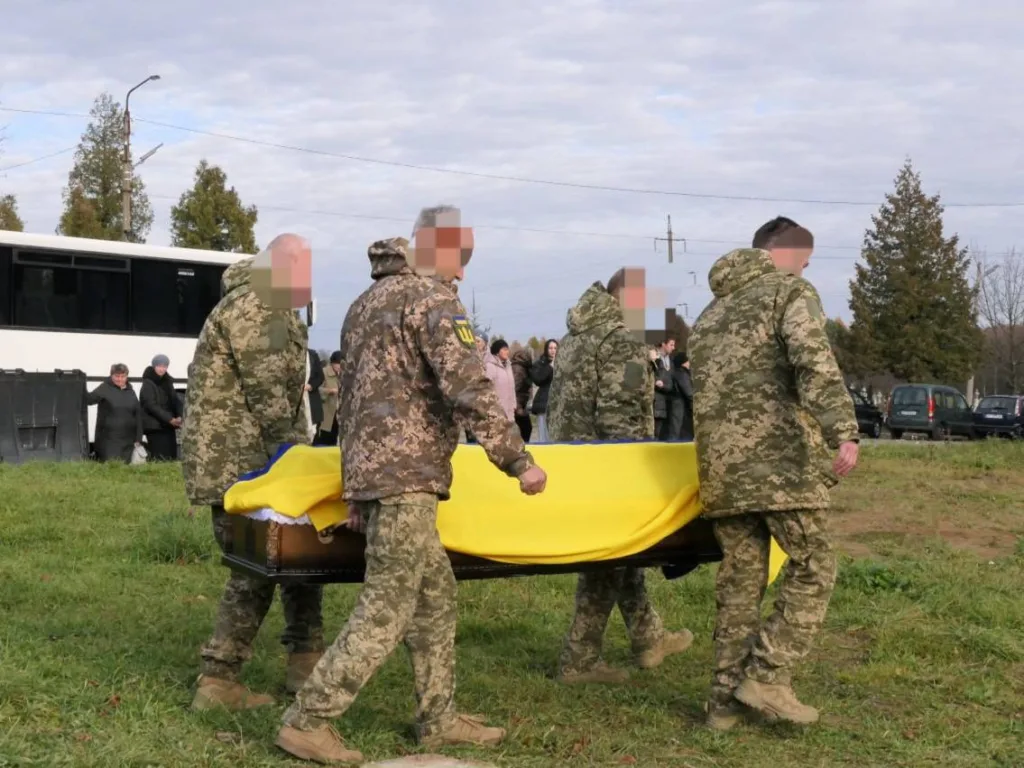 Військові несуть труну, вкриту українським прапором