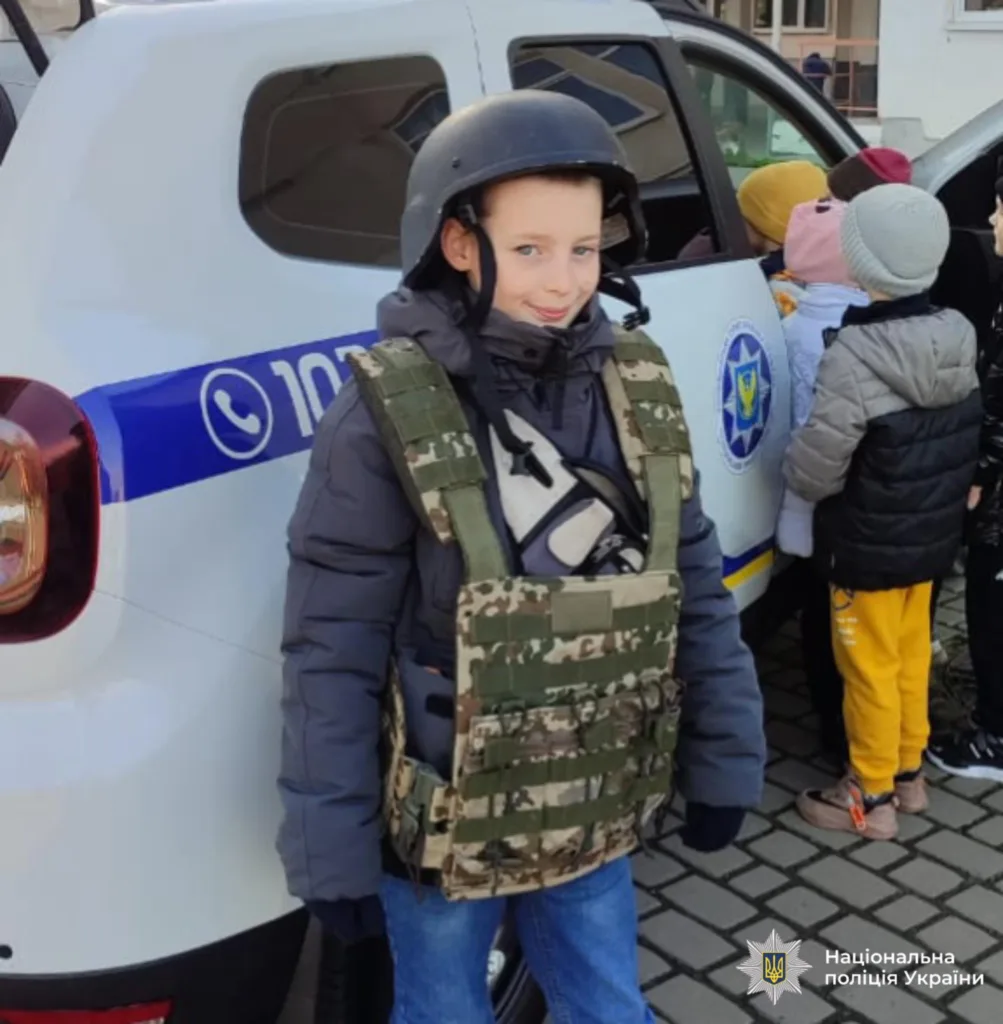 Дитина у бронежилеті біля поліцейського авто