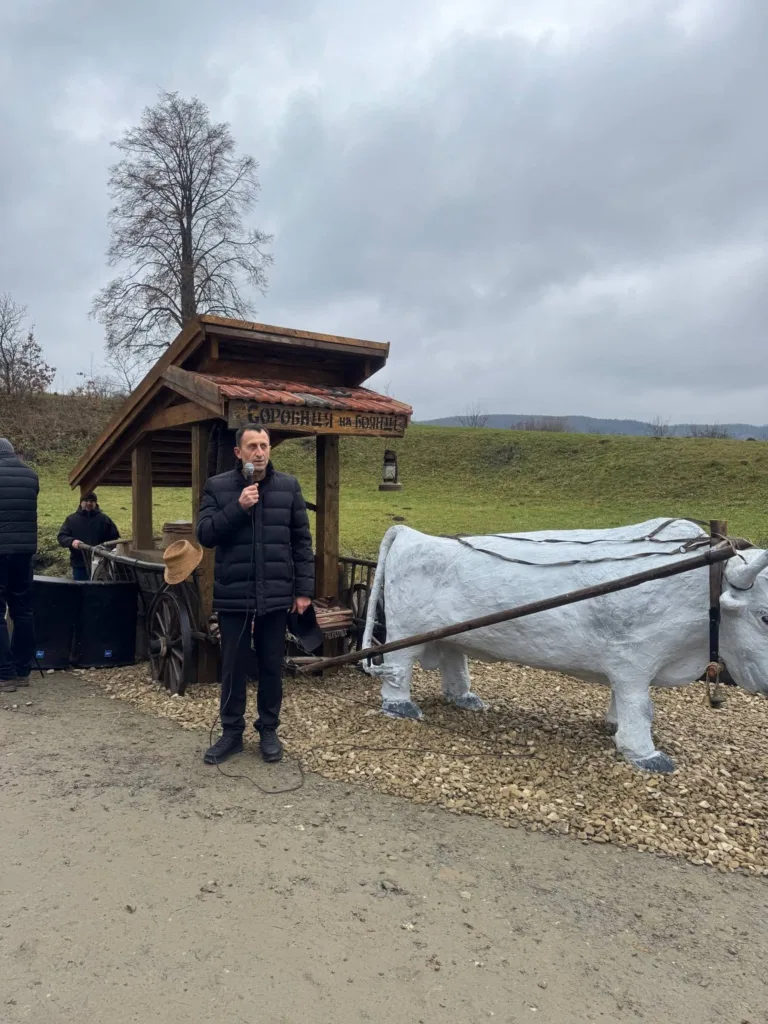 Чоловік говорить біля дерев’яного воза й фігури бика