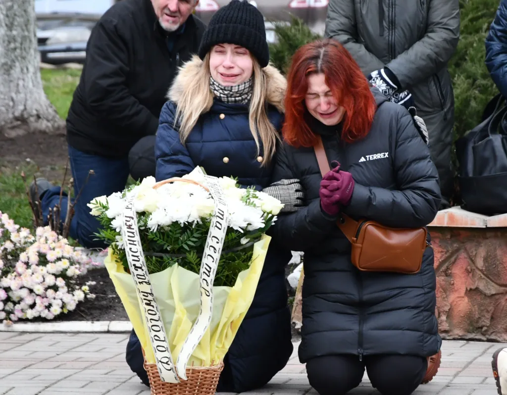 Люди плачуть і тримають квіти на вшануванні