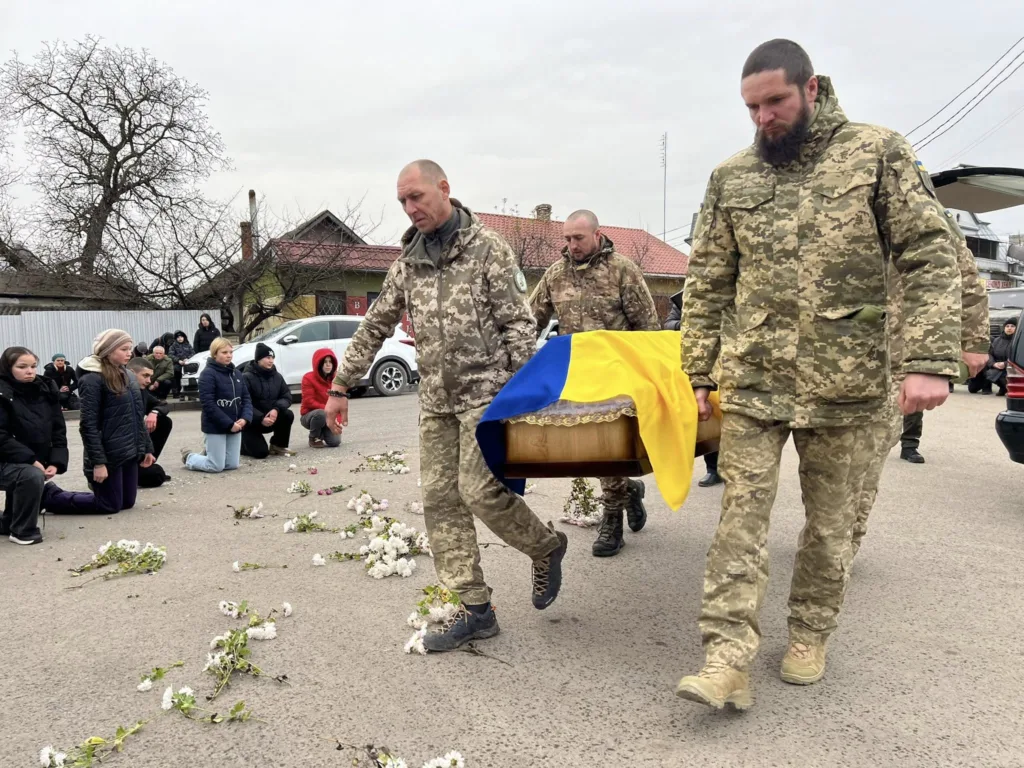 Військові несуть труну, люди стають на коліна