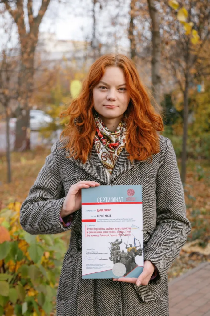 Жінка тримає сертифікат на вулиці восени