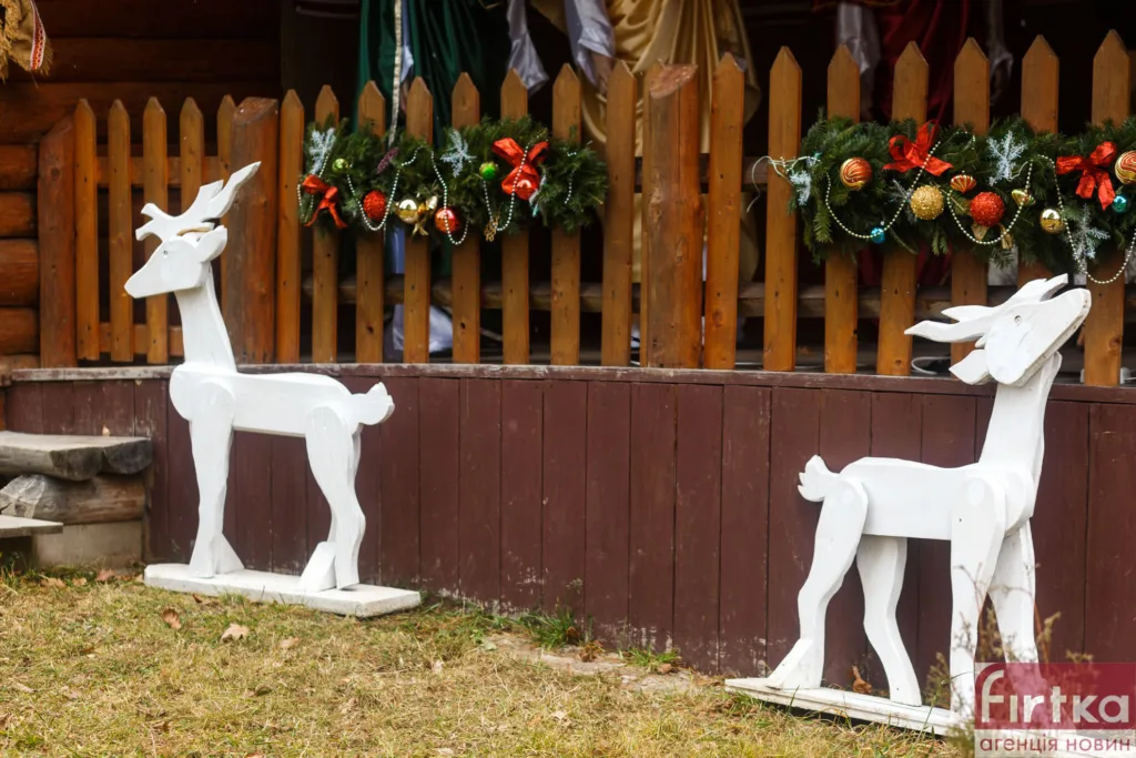 Дерев'яні олені біля різдвяно прикрашеного паркану