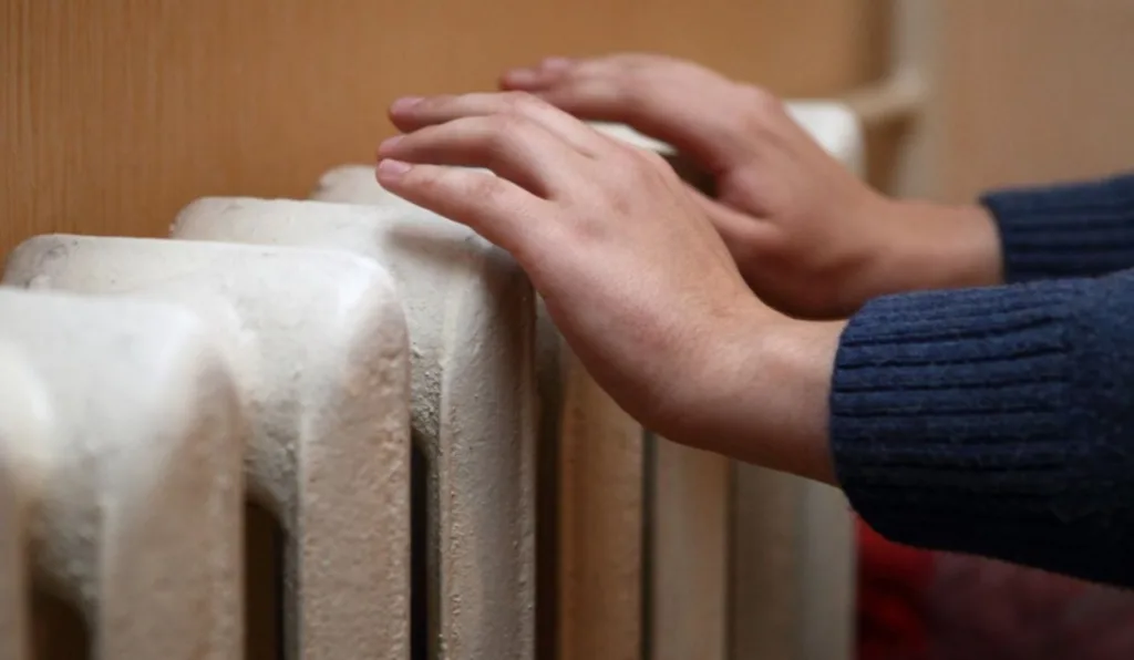 Руки гріються біля батареї опалення