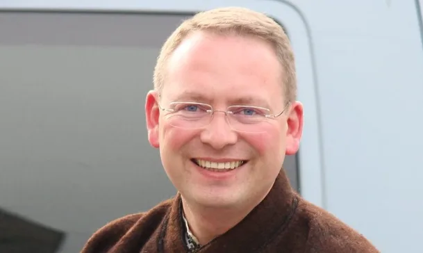 Усміхнений чоловік у коричневому светрі біля автомобіля