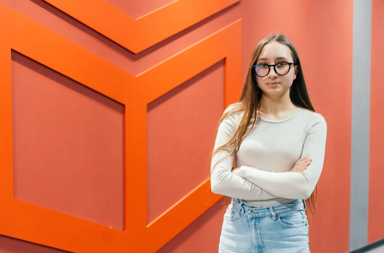 Молода жінка стоїть біля червоної стіни