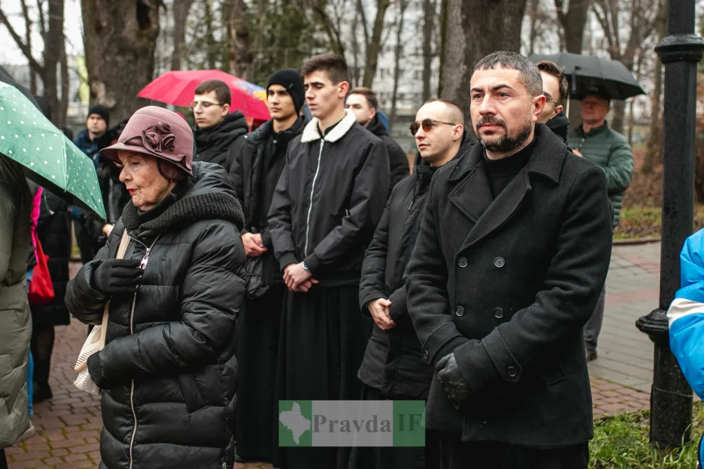 Люди стоять на вуличному заході під парасолями