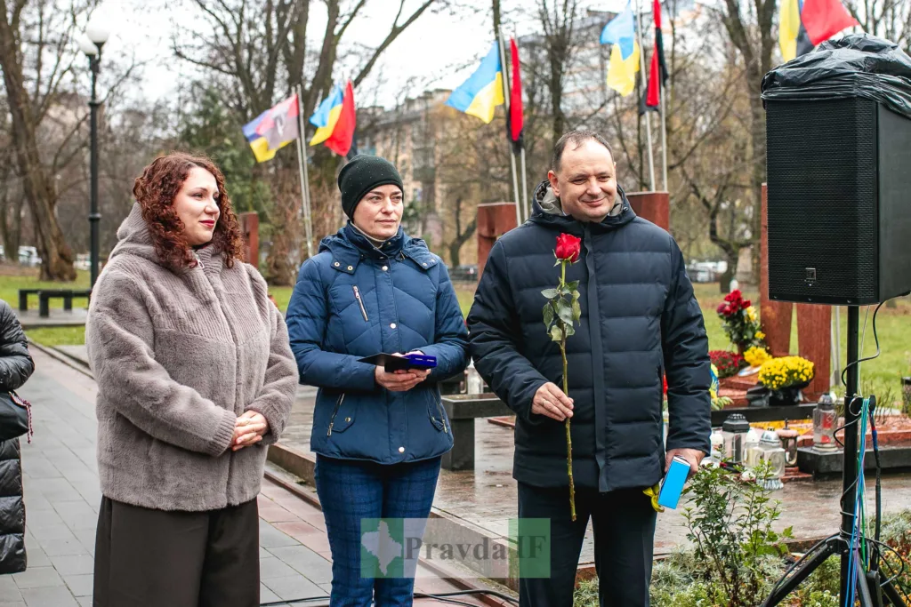 Люди на меморіальному заході з квітами та прапорами