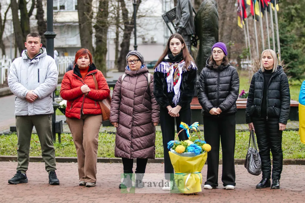 Люди стоять біля пам'ятника з квітами