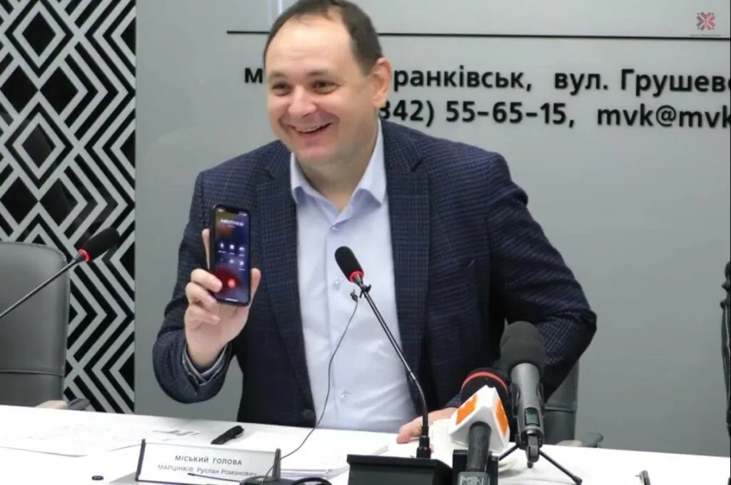 Чоловік посміхається і тримає телефон на пресконференції