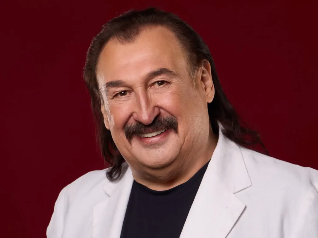 Усміхнений чоловік у білому піджаку на червоному фоні