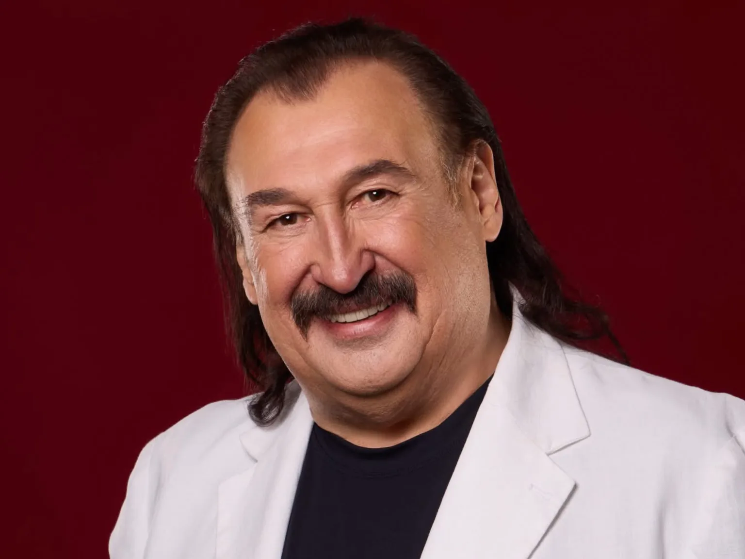 Усміхнений чоловік у білому піджаку на червоному фоні