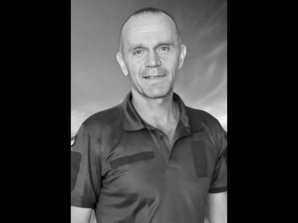 Чоловік у футболці посміхається на сірому тлі