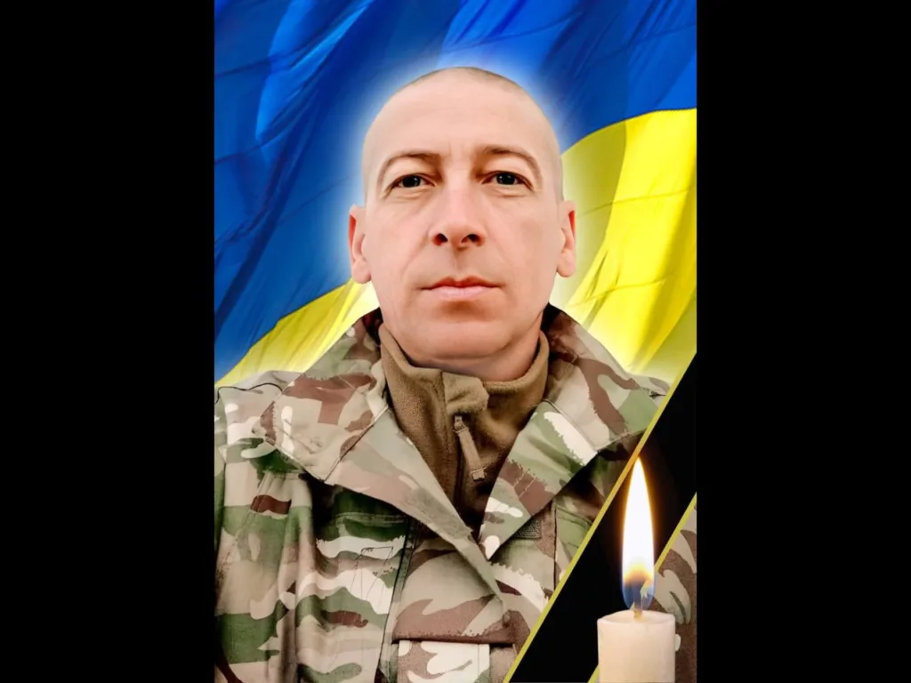 Військовий перед прапором України та запаленою свічкою