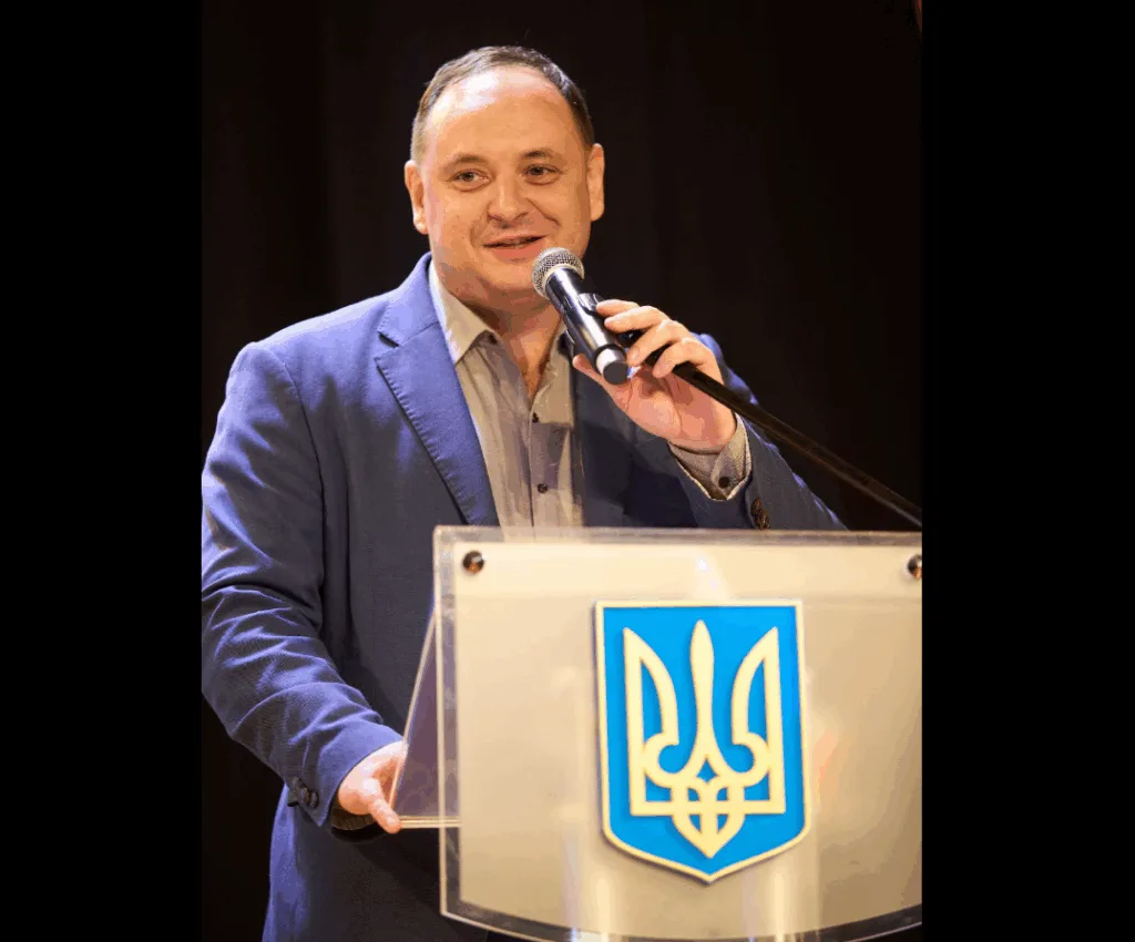 Чоловік виступає за трибуною з гербом України