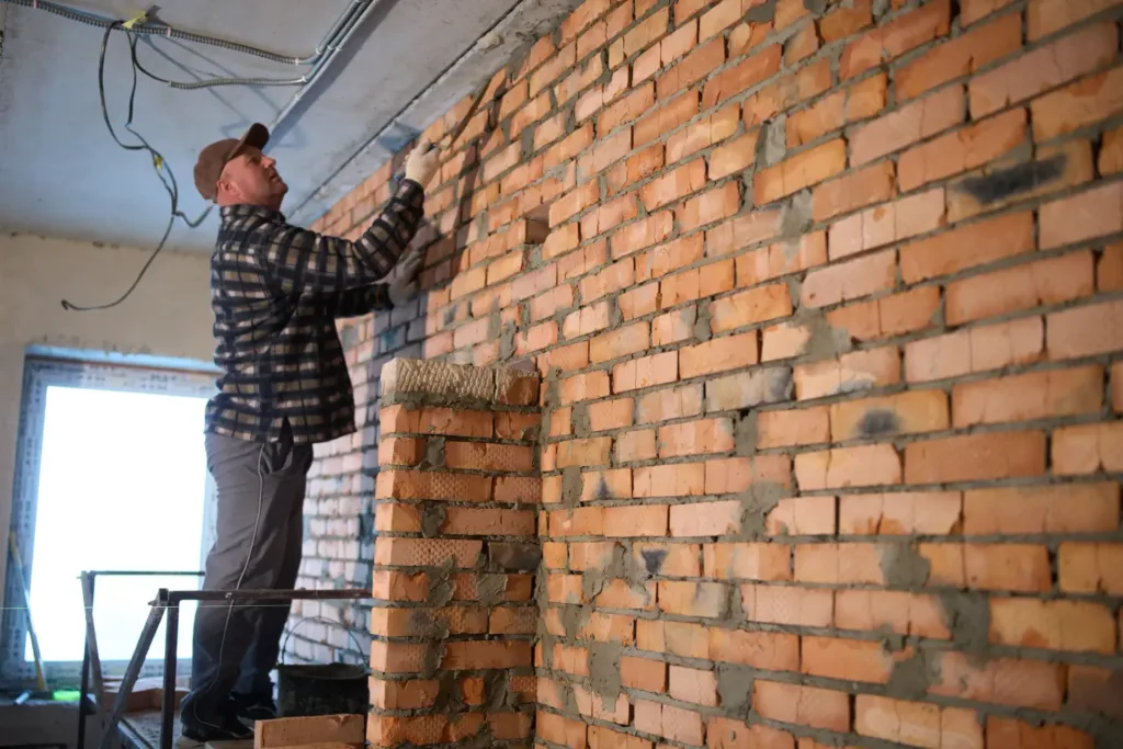 Робітник ремонтує цегляну стіну всередині будинку