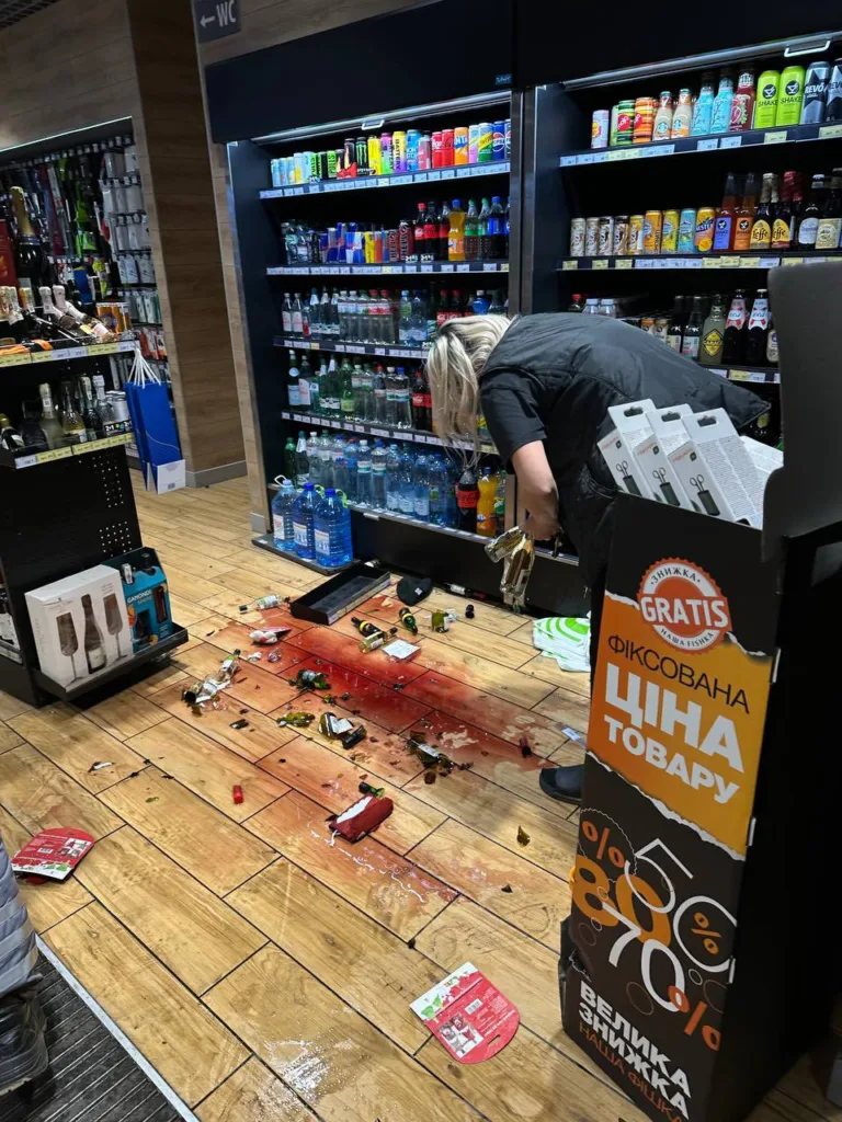 Працівниця магазину прибирає розбиті пляшки біля холодильника