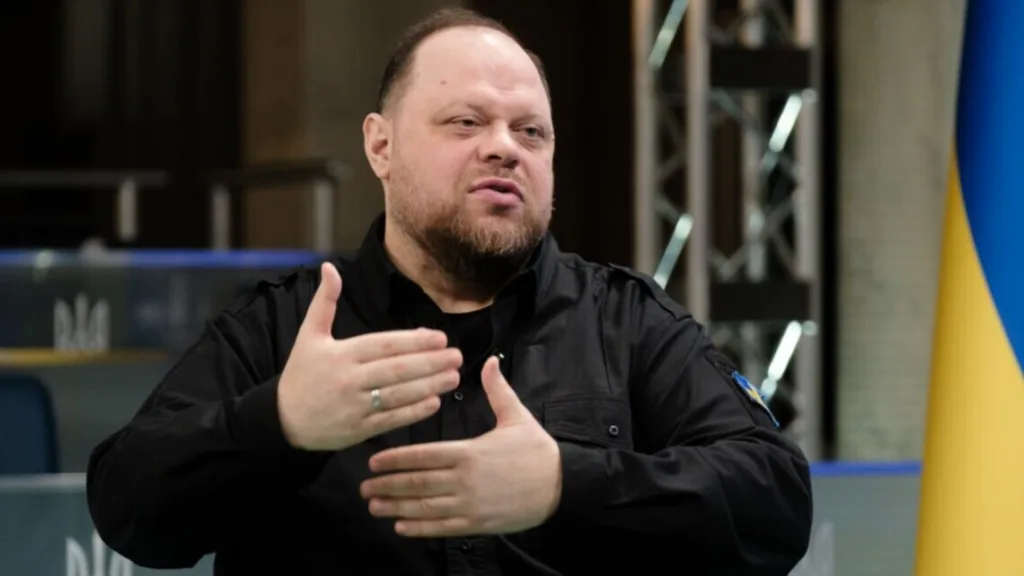 Чоловік у чорній сорочці говорить біля прапора України