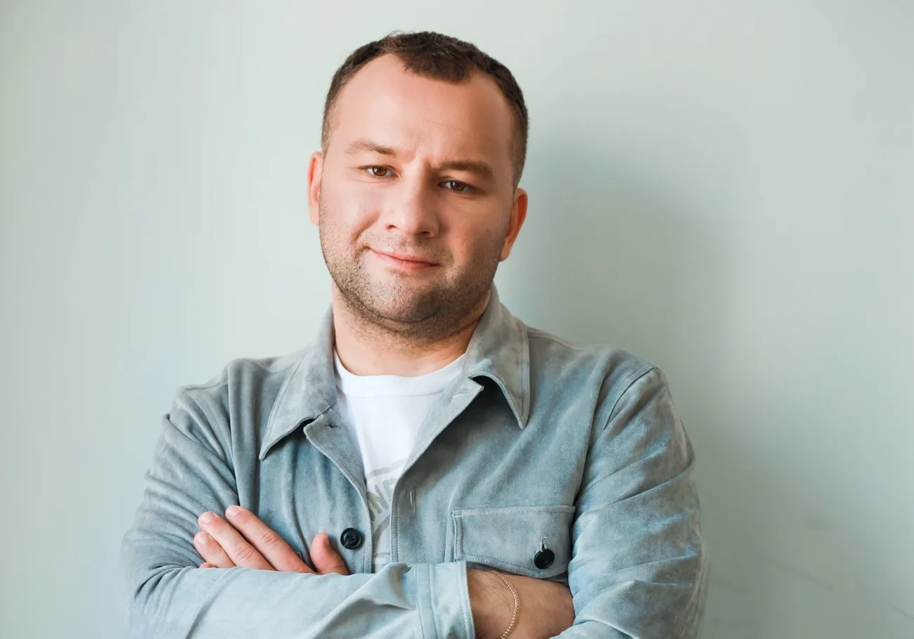 Усміхнений чоловік у сірій сорочці стоїть