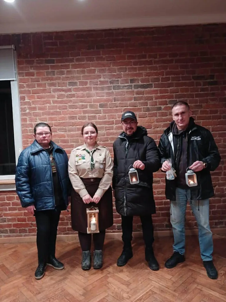 Люди тримають ліхтарі зі свічками біля цегляної стіни