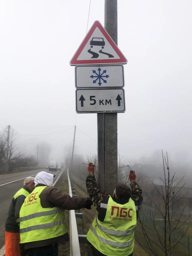 Робітники встановлюють знак слизька дорога взимку