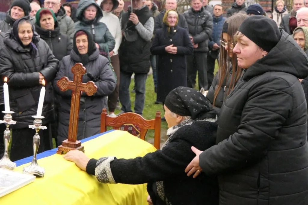 Люди прощаються біля труни, накритої українським прапором