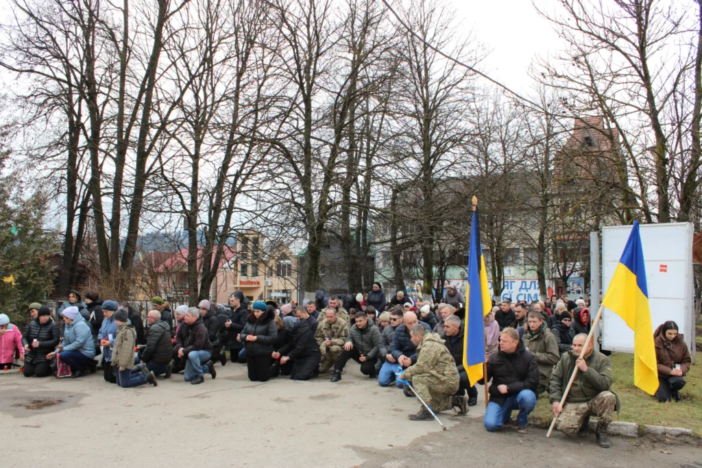 Люди на колінах з українськими прапорами
