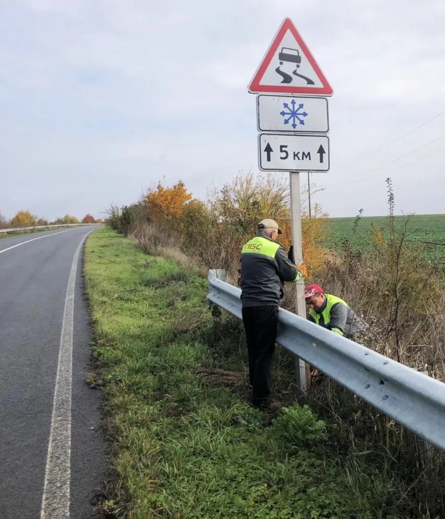 Робітники встановлюють дорожній знак слизька дорога