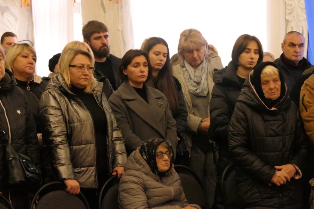 Люди стоять у скорботі під час церемонії прощання