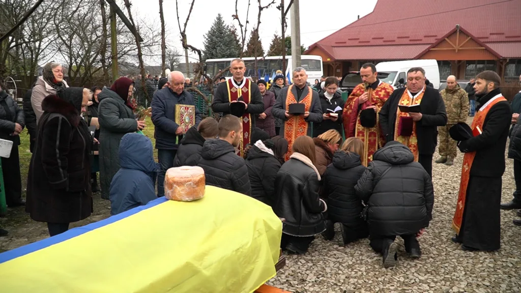 Похоронна церемонія з українським прапором та священниками