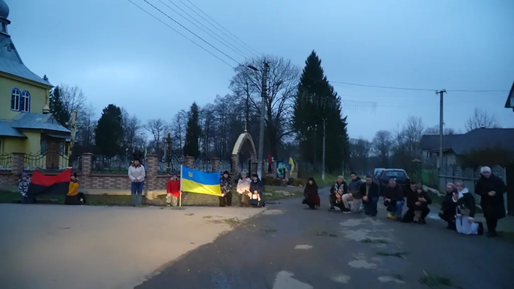 Люди з українським прапором стоять на колінах на вулиці