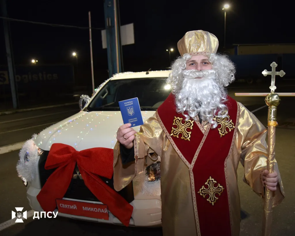 Святий Миколай тримає український паспорт біля авто