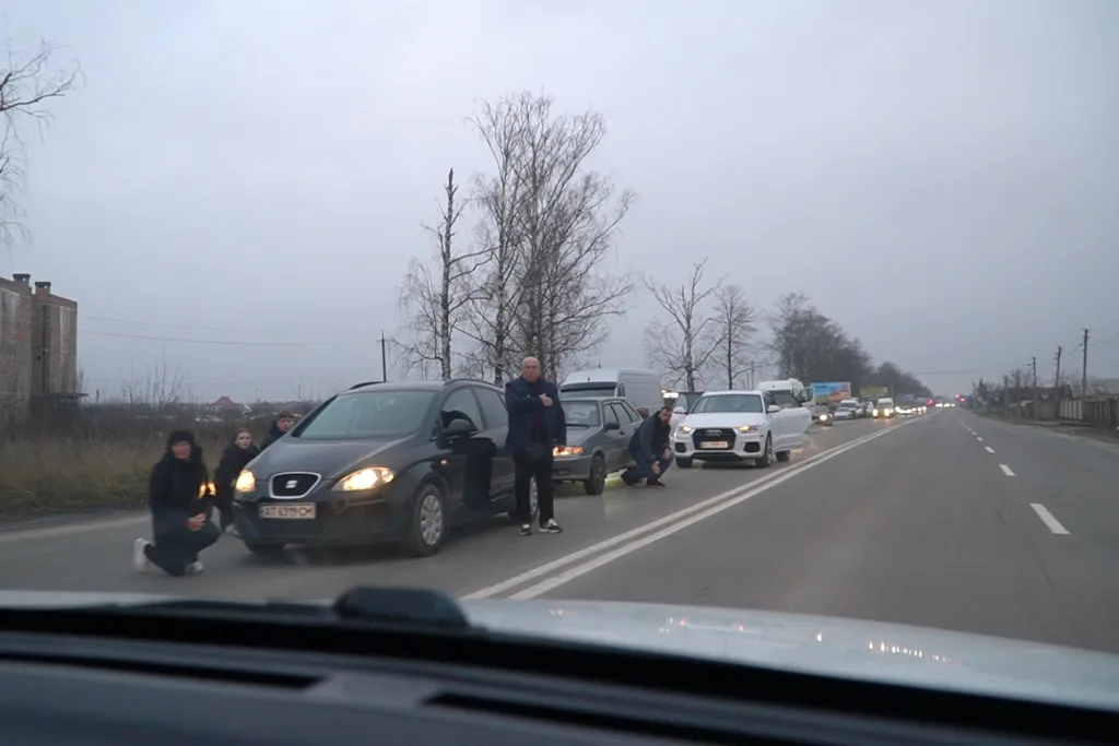 Люди стоять біля автомобілів на дорозі