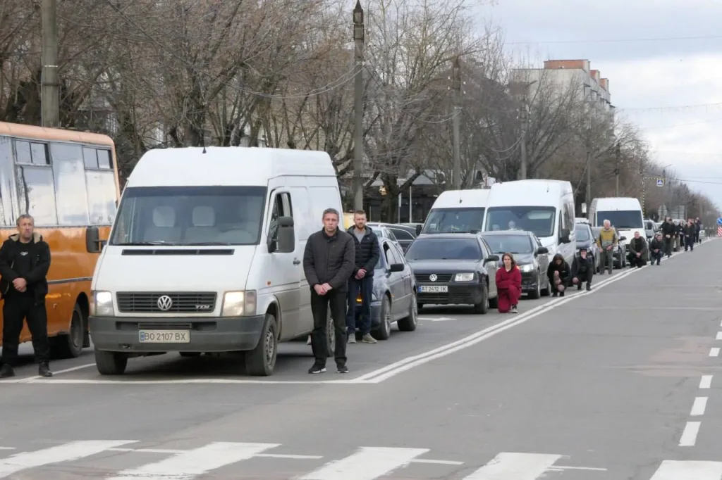 Люди стоять і стоять на колінах біля дороги