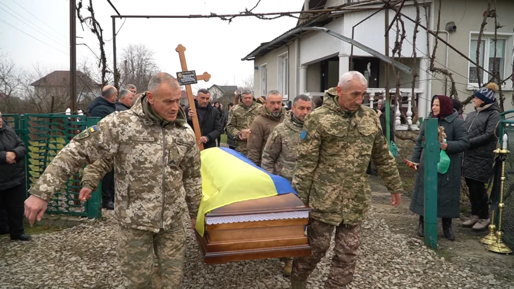 Військові несуть труну, покриту українським прапором