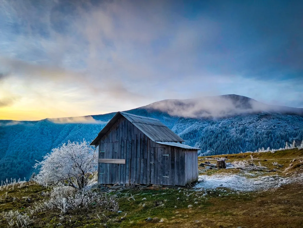 Дерев’яна хата в засніжених горах на світанку