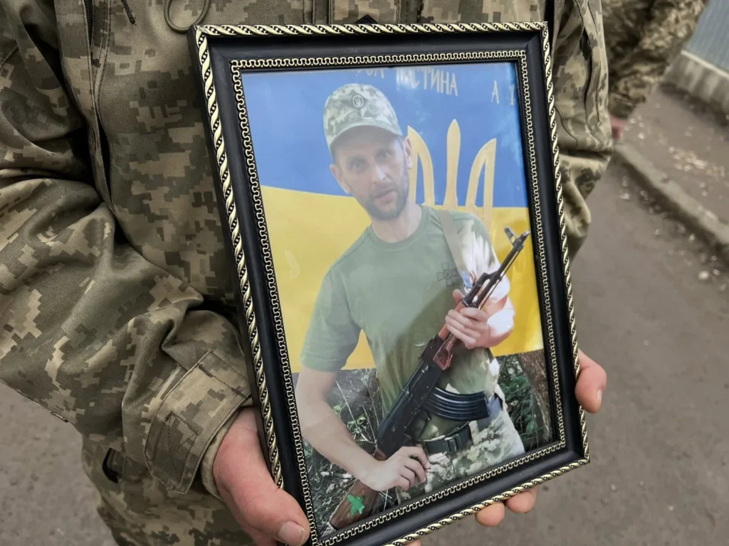 Військовий тримає фото солдата перед прапором України