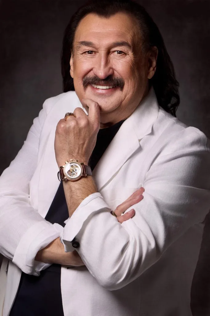 Чоловік у білому піджаку з годинником посміхається