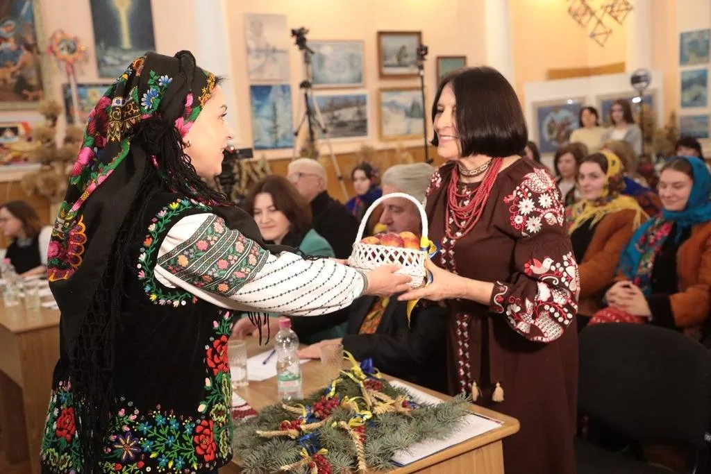 Жінки в народному вбранні обмінюються кошиком яблук