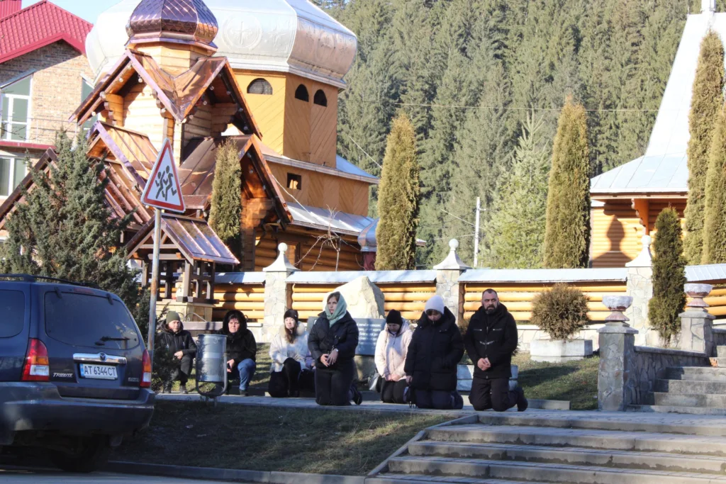 Люди моляться біля дерев’яної церкви в горах