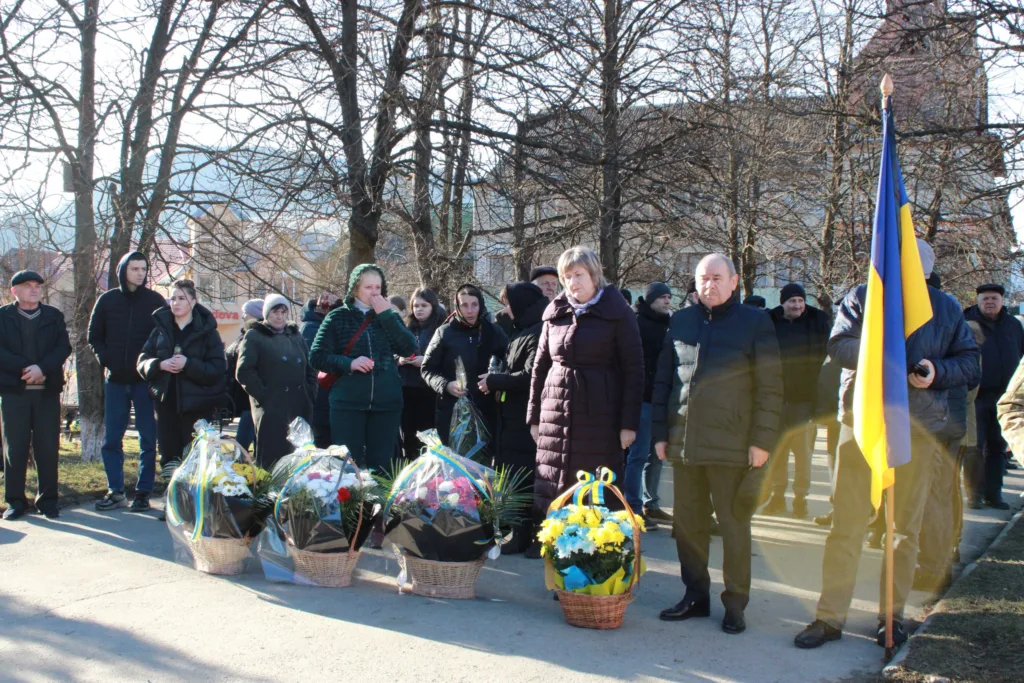 Люди з квітами біля українського прапора на вулиці