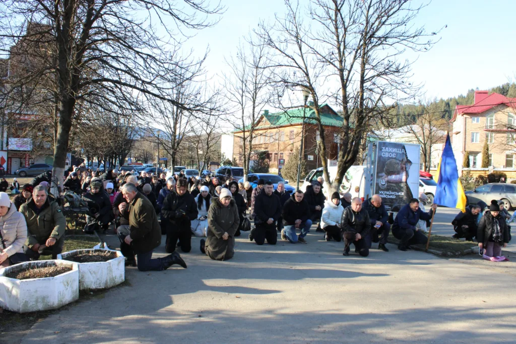 Люди на колінах із українським прапором на вулиці