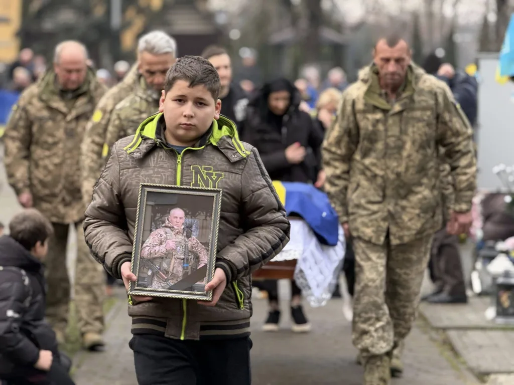 Хлопчик несе фото загиблого військового на похороні