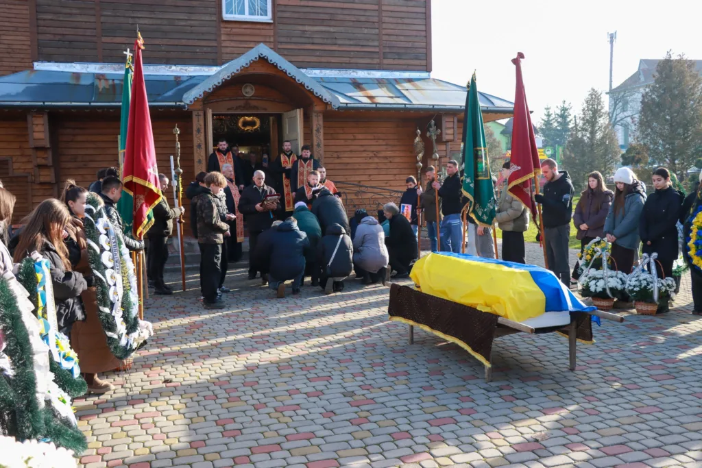 Похоронна церемонія перед церквою з українським прапором