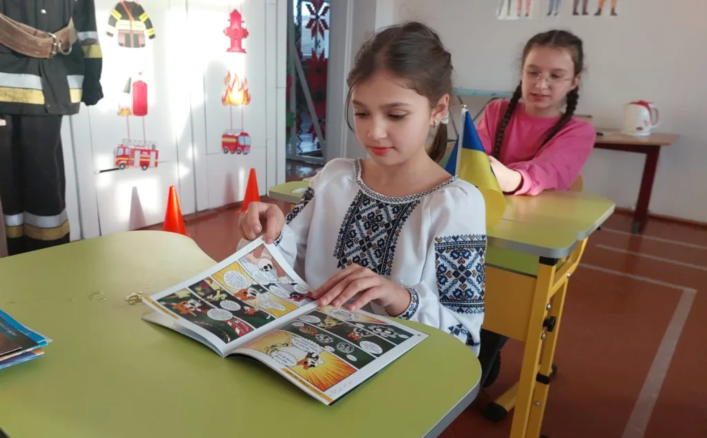 Дівчинка читає комікс у класі з прапором України