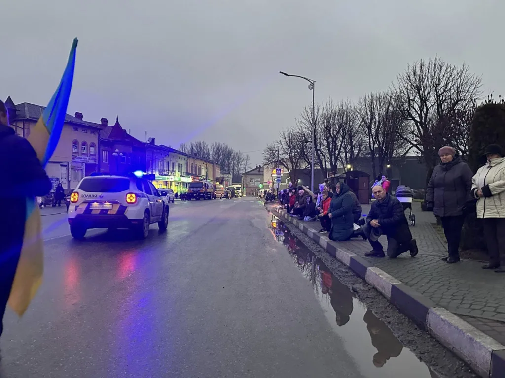 Люди стоять уздовж дороги з поліцейським авто