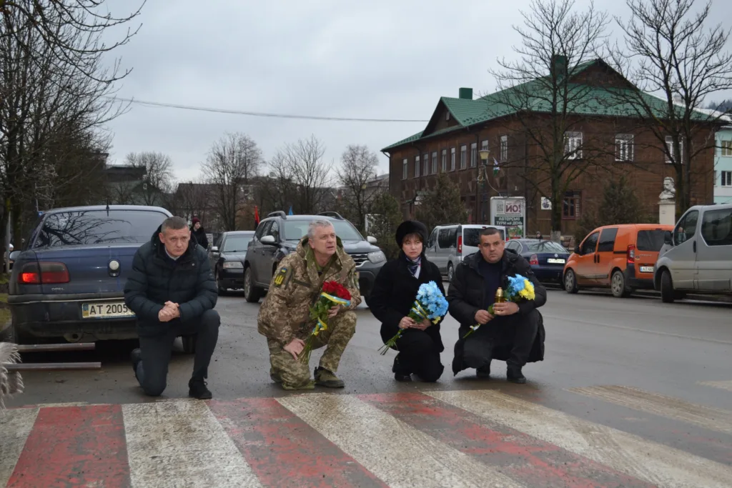 Люди на колінах з квітами на вулиці