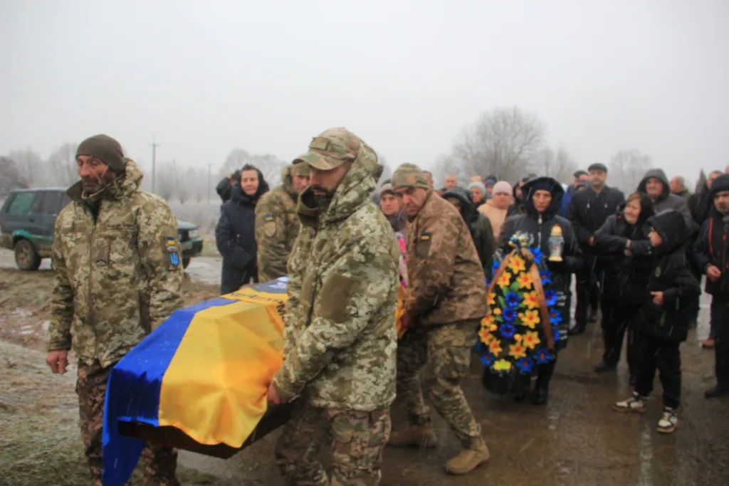 Військові несуть труну, накриту українським прапором